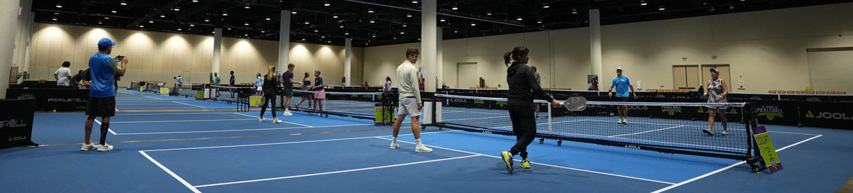 People playing pickleball on blue indoor courts with JOOLA nets.