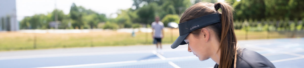 Woman wearing a black JOOLA visor on a blue pickleball court